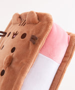 Top view of the squisheen plush shows off Pusheen’s brown face and four paws. Pusheen plush lies on a white surface.  