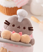 Pink Biscuit Baker Plush is a grey cat wearing a bakery outfit that's accented by pink details and white chef's hat.