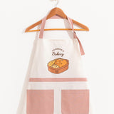 Front view of a white apron and dusty pink straps and pocket details. Both the neck ties and back straps are adjustable. 