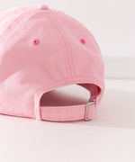 Close-up view of the buckle adjustment strap on the back of the cap. The buckle strap hat seams matches the light pink color hat color while the eyelet holes are a slightly darker pink color.  