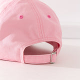 Close-up view of the buckle adjustment strap on the back of the cap. The buckle strap hat seams matches the light pink color hat color while the eyelet holes are a slightly darker pink color.  