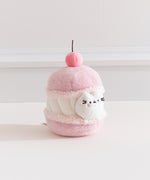 Side quarter view of the cherry macaron Pusheen plush. The macaron plush has a light pink shells with a white whipped filling in the middle. 