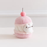 Side quarter view of the cherry macaron Pusheen plush. The macaron plush has a light pink shells with a white whipped filling in the middle. 