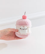 Model's hand holding Pusheen Sweets Cherry Macaron Plush 2-pc Environment. The cherry macaron plush has a layered cylinder base with a 3D cherry.