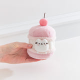 Model's hand holding Pusheen Sweets Cherry Macaron Plush 2-pc Environment. The cherry macaron plush has a layered cylinder base with a 3D cherry.