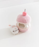 Pink plush toy resembling a macaron with a small white Pusheen the cat sitting next to the macaron plush on a light background.