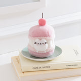 Pink plush toy resembling a macaron with a cherry on top, sitting on a stack of books.