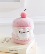 Side quarter view of the cherry macaron Pusheen plush. The macaron plush has a light pink shells with a white whipped filling in the middle. 