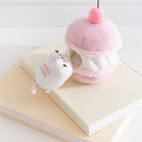 Side view of the Cherry Plush. The removable interior plush rests in front of the macaron environment. The little white cat plush has light pink embroidery details.  