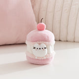 Cat plush toy resembling a macaron with a cherry on top, sitting on a light pink surface. A white Pusheen the Cat mini plush is able to removed from the macaron plush environment. 