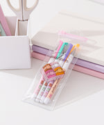 Pusheen Sweets Gel Pen set lies on a white notebook. The four pens have pink, green, purple, and orange barrels with pusheen macaron graphic patterns.