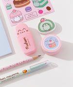 Close-up view of the contents of the Pusheen Sweets Stationery set. The pencil, pen, stickers, eraser, pencil sharpener, and highlighter include graphics and prints of Pusheen the Cat as various sweet dessert characters and flavors including a strawberry, lavender, chocolate, matcha, vanilla, and cherry.