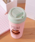 Sweets Pusheen Travel Mug on a desktop with a chocolate cupcake next to the pink Pusheen cup.