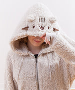 Model sitting on a wooden floor, wearing the Pusheen Character Hoodie with the hood pulled up. The model is smiling while daydreaming. 
