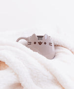 The box packaging for the Pusheen Character Mug in front of a white background. The box is a pink cardboard square that cover the mug entirely. On the front of the box is the Pusheen logo, a photo of the mug inside, and the name ‘Ceramic Mug’ printed underneath it in English and French. The top and side of the box features the Pusheen the Cat Logo.