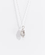 Sterling silver finish of Pusheen Dipped Cone Charm Necklace in its white packaging box. The necklace is hanging inside the white box with a pink, white, and purple informational card. 
