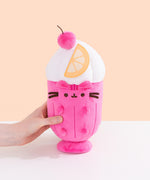 Back view of the Pusheen Fruits Fruit Parfait Plush. The bottom two-thirds of the plush is a hot pink color that tapers to a smaller base while the top portion of the plush of is a swirl of a fuzzy whipped plush topping. 