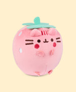 Back view of the Pusheen Fruits Strawberry Squisheen Plush. On the back of the light pink squisheen is Pusheen’s signature back stripes duo embroidered in dark pink. Under the stripes is Pusheen’s striped tail in alternating pink colors. Coming off the top of the plush are green felt leaves and a stem. 