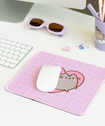 The pink with white grid pattern Pusheen Mouse Pad sits in front of its purple packaging. The packaging shows the size of the mouse pad as well as listing its features: waterproof, durability, precision, and speed. 