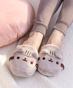 Model wearing the Pusheen Plush Slippers, wearing loose grey pajama pants and standing on top of a wooden floor.