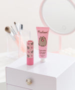Hand lotion and Pusheen lip balm sit on a vanity. The set has pink packaging and is small enough to carry in a purse. 