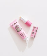 Lip balm and lotion lie on a white desktop. The Pusheen-themed set has a strawberry scented lotion. 