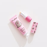 Lip balm and lotion lie on a white desktop. The Pusheen-themed set has a strawberry scented lotion. 