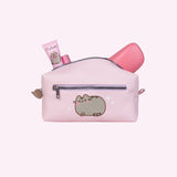 Back view of the Pusheen cosmetic bag. Various pink accessories stick out of the top of the bag. The back has an exterior zipper above a graphic of Pusheen blushing with her front paws crossed. 
