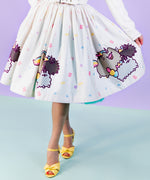 Closeup view if printed Pusheenicorn pattern skirt pattern. White skirt is dotted with pastel pink, purple, blue and yellow magical jewels with a repeating border pattern of Pusheenicorn carrying a pink cupcake in her mouth while walking alongside her and friends. 