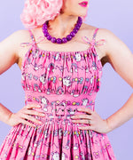 Front view of smiling model wearing Super Pusheenicorn Dreamer Dress while holding a medium-size plush of Pusheen the Cat in their hands.  